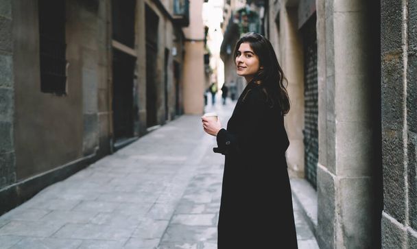 Half length portrait of attractive female tourist with takeaway cup looking at camera during coffee time on sightseeing, beautiful Caucasian girl 20 years old posing while exploring city streets - Foto, Imagem