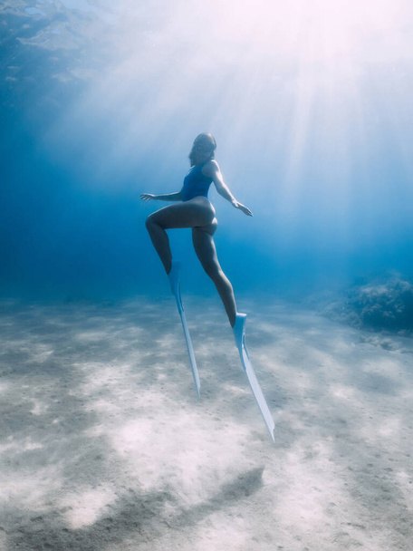 Female free diver with fins posing underwater in blue sea with sunlight. - Photo, Image