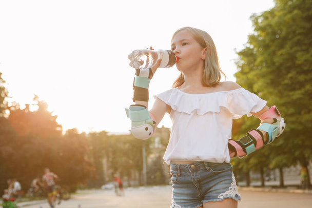 Young beautiful girl drinking water while rollerblading in the city, copy space - Фото, зображення
