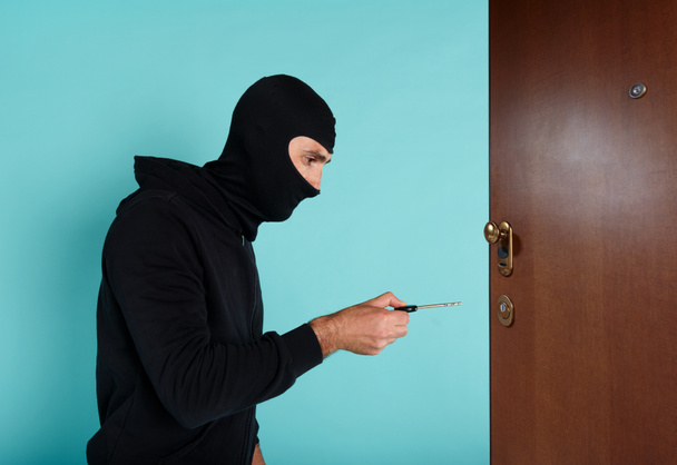 Tolvaj maszkkal megpróbálja kinyitni a lakás ajtaját egy kulccsal. - Fotó, kép