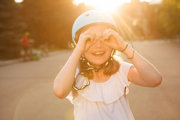 Excited young girl in rollerblading helmet laughing looking to camera through imaginary hand binoculars - 写真・画像