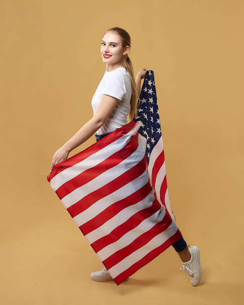 attractive blonde poses with an American flag. photo shoot in the studio on a yellow background. - Fotografie, Obrázek
