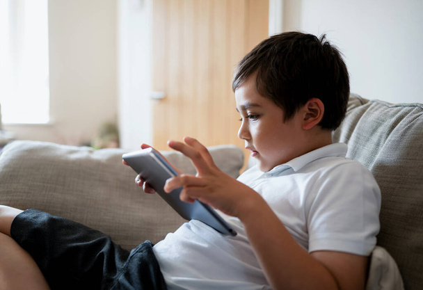 Niño de la escuela usando tableta que estudia en línea en Internet, niño jugando o viendo dibujos animados en la almohadilla digital, niño feliz relajándose en casa, niños con tecnología y concepto de red social - Foto, imagen