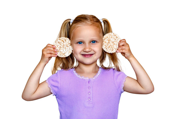 Little girl holding rice cookies near her ears. A child on a white background holds round waffles near her ears - Foto, immagini