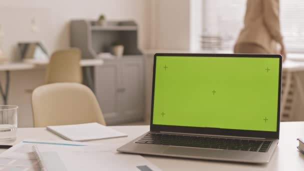 Inclinazione a sinistra del computer portatile con chiave cromatica sullo schermo sulla scrivania in ufficio di giorno, donna irriconoscibile con documenti che camminano sullo sfondo - Filmati, video