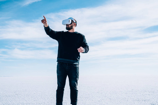 Bearded male hiker wearing casual outfit using virtual reality goggles while travelling in natural environment in Bonneville Salt Flats United States - Foto, Imagen