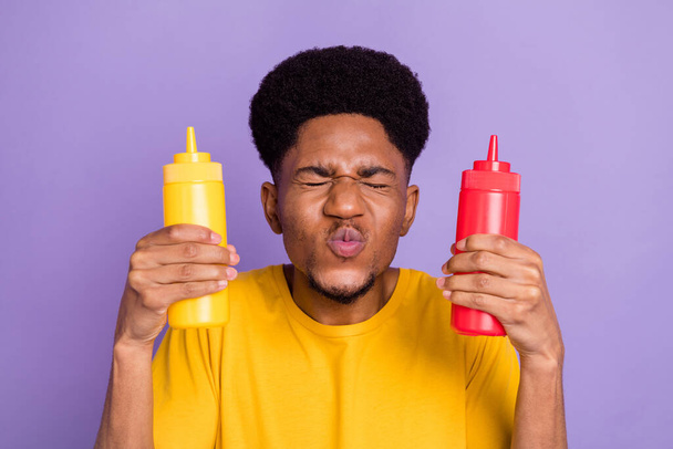 Photo de funky jeune afro américain heureux homme tenir ketchup moutarde envoyer baiser d'air isolé sur fond de couleur violette - Photo, image