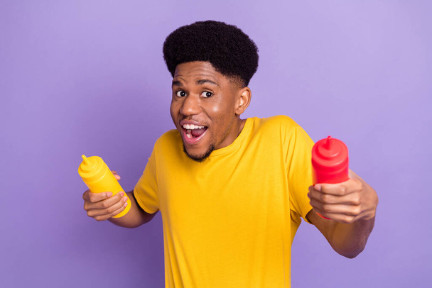 Portrait of attractive playful cheerful guy holding ketchup bottles having fun fooling isolated over violet purple color background - Foto, Bild