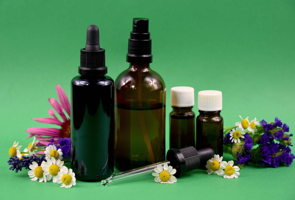Glass brown cosmetic bottles with flowers and herbs stock images. Vial with essential oil and flower extract still life stock photo. Spa and wellness setting images - Photo, Image