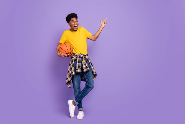 Full body photo of young afro american man wear denim jeans point finger empty space basketball isolated on violet color background - Фото, зображення