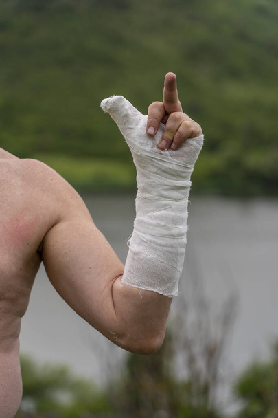 A male hand in a plaster cast sign of middle finger point upward with nature background, close up - 写真・画像