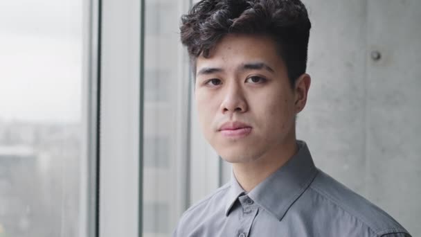 Portrét vážný mladý asijský chlap korejský japonec pracovník číňan obchod muž student dívá ven okno stojící v kanceláři vnitřní myšlení snění plánování při pohledu na kameru usmívající se zubatý - Záběry, video
