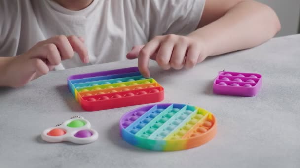 unrecognizable child pushes bubbles on colorful poppit toy with fingers at table - Footage, Video
