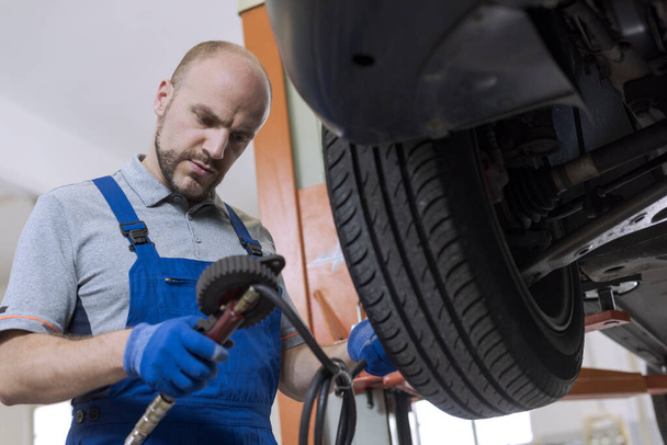 Mechanic inflating a tire and checking air pressure with a pressure gauge at the auto repair shop - Фото, зображення