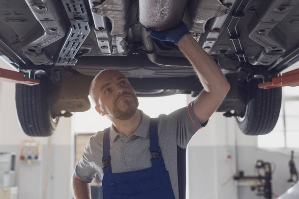 Professional mechanic working under a car in a repair shop, car maintenance and repair concept - Foto, Bild