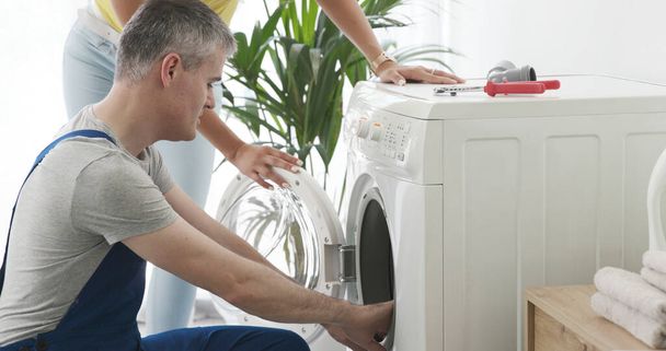 Technician repairing a washing machine at home, he is checking the gasket - Foto, imagen