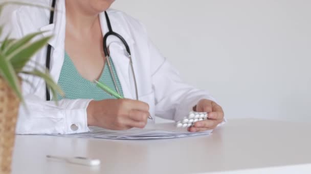 認識できない女性の医者は彼女の机に座っている薬のための処方を準備します - 映像、動画