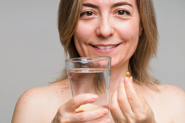 Heureuse femme caucasienne mature avec une bonne nutrition prenant des pilules vitaminées avec un verre d'eau pour maintenir un mode de vie sain - Photo, image