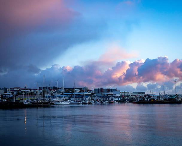 HAFNARFJORDUR, ISLÂNDIA - 16 de julho de 2021: Pôr do sol no porto de pesca de Hafnarfjordur. Nuvens cor de rosa no céu. Veleiros, pequenos barcos de pesca e edifícios portuários. Islândia.  - Foto, Imagem