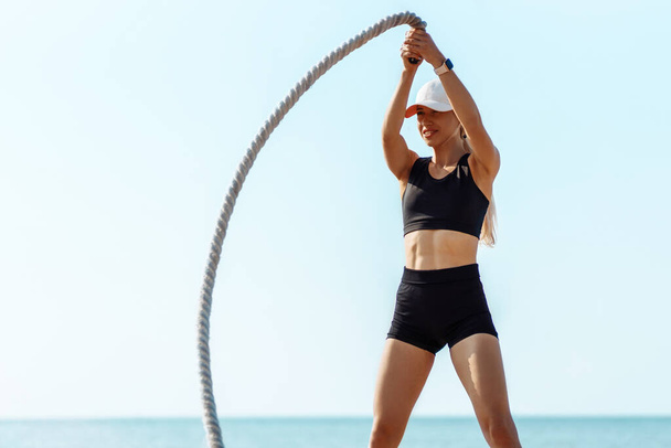 Fitness woman using training ropes for sports, on the beach at sunrise, Athlete exercising with fighting ropes, exercising by the sea, enjoying the fresh morning air, Sport health concept - Foto, imagen