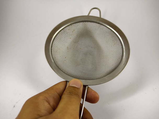 foto de una mano sosteniendo un colador de acero inoxidable aislado sobre un fondo blanco - Foto, imagen