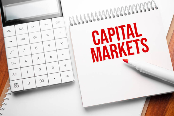 Notepad with text Capital Markets on wooden background with calculator and red marker - Foto, imagen