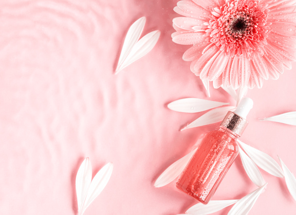 Cosmetische schoonheid serum olie zuur fles product op roze achtergrond in water met roze madeliefje - Foto, afbeelding