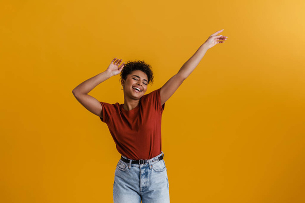 Happy casually dressed young african woman standing over yellow wall background, dancing - Valokuva, kuva