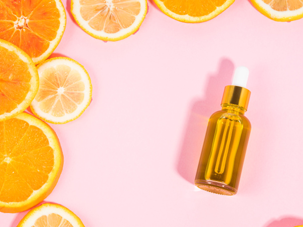 オレンジの柑橘類のスライスとピンクの背景にドロッパーとビタミンC血清ボトル - 写真・画像