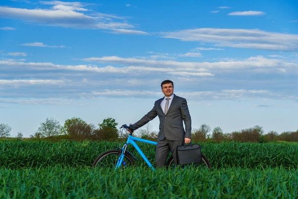 ビジネスマンは緑の芝生のフィールドで自転車に乗る-自由、休暇やフリーランスのためのビジネスコンセプト。美しい春の自然. - 写真・画像