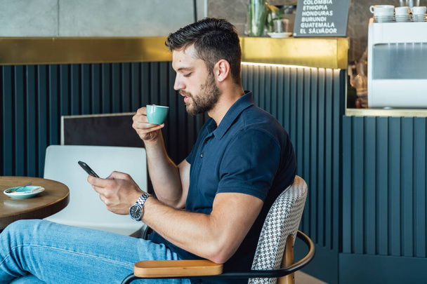 Komea liikemies Kahvin juominen ja matkapuhelimen käyttö kahvilassa.Menestyvä liikemies nauttii espressokahvistaan ja tekstiviestien kirjoittamisesta puhelimessa istuessaan ja työskennellessään ravintolassa. - Valokuva, kuva