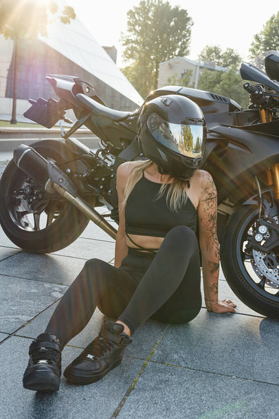 Tattooed woman biker with black motorcycle on city street - Photo, Image