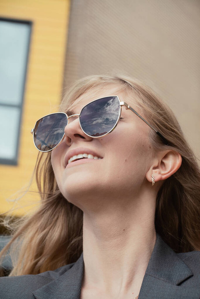 Portrait of young cheerful woman in sunglasses reflecting clouds - Photo, Image