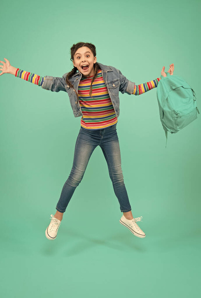 Happy energetic child jump with school bag in casual fashion style blue background, childhood - Valokuva, kuva