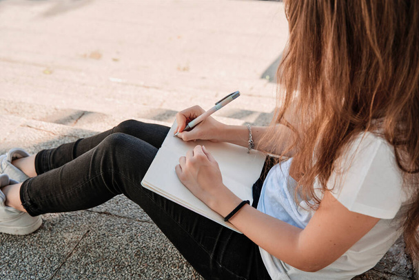 Unrecognizable woman sitting on stairs on a sunny day studying outdoors. Concept of education - Foto, Imagen