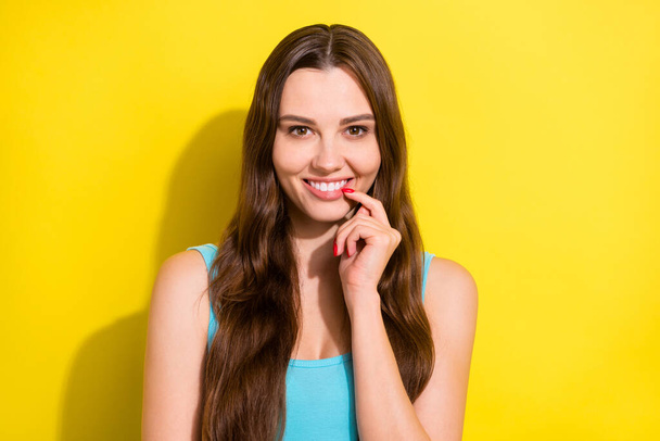 Photo portrait smiling happy girl with long hair in blue singlet touching lips isolated bright yellow color background - Foto, afbeelding