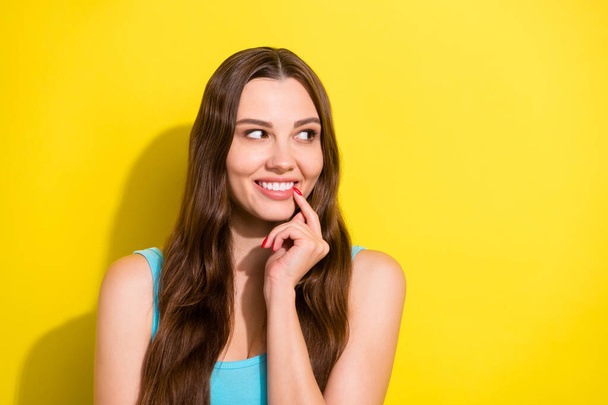 Portrait of attractive cheerful girl biting nail guessing copy blank space ad isolated over bright yellow color background - 写真・画像