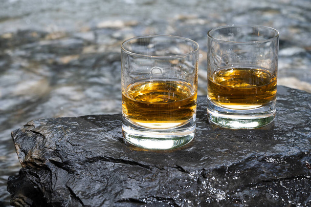 Glas starken Scotch Single Malt Whisky mit schnell fließenden Gebirgsfluss im Hintergrund, Schottland - Foto, Bild