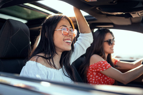Shot of pretty young women singing while driving a car on road trip on beautiful summer day. - Foto, Imagen