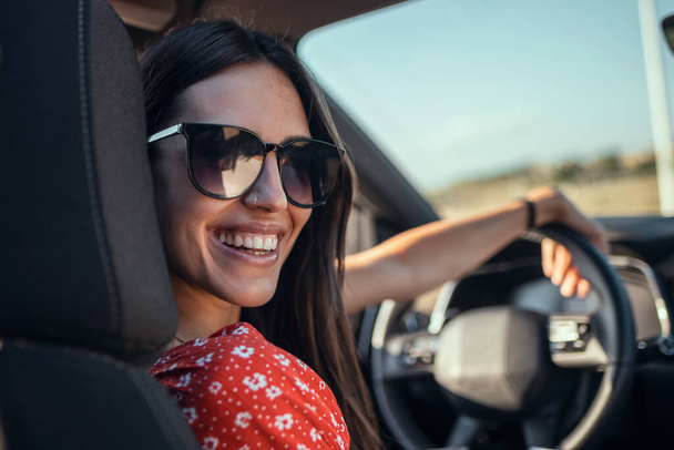 Portrait of beautiful young woman driving a car while smiling to the camera. - Foto, Imagen