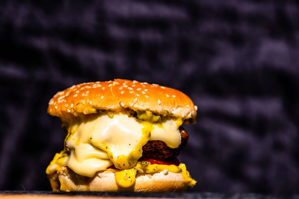 An appetizing fresh burger with melted cheese on black background - Zdjęcie, obraz