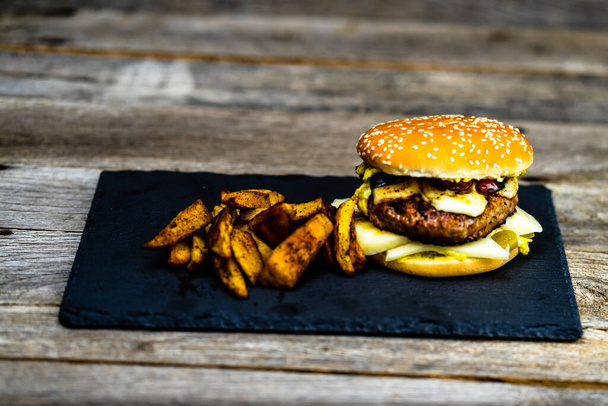 A tasty homemade burger with fried potatoes on a wooden table - Foto, Imagen