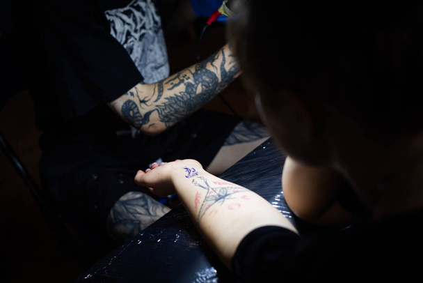 bijgesneden schot van het tatoeëren proces bij de hand in de salon. Een professionele tatoeëerder introduceert inkt in de huid met behulp van een naald van een tattoo machine.Professional tatoeëerder werken in studio. - Foto, afbeelding
