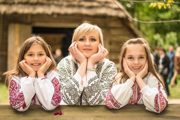 Una hermosa mujer con dos hijos hijas retrato vestido con camisas bordadas en el fondo de la casa de paja, sonriendo. Día de la Independencia de Ucrania, Día del Bordado, Día de la Madre. - Foto, Imagen