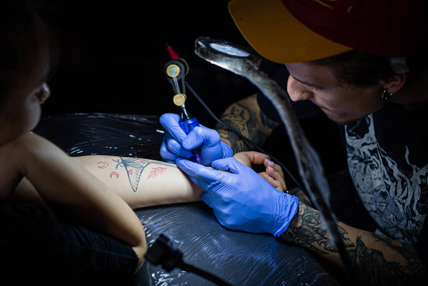 Kuaförde dövmenin kesilip atılmış hali. Profesyonel bir dövme sanatçısı dövme makinesinin iğnesini kullanarak cilde mürekkep yerleştirir. Stüdyoda çalışan profesyonel bir dövmeci.. - Fotoğraf, Görsel