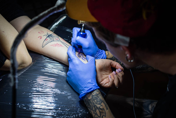 recortado tiro de proceso de tatuaje en la mano en el salón. Un artista profesional del tatuaje introduce tinta en la piel usando una aguja de una máquina de tatuaje.Tatuaje profesional que trabaja en el estudio. - Foto, imagen