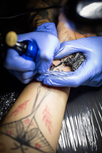 Kuaförde dövmenin kesilip atılmış hali. Profesyonel bir dövme sanatçısı dövme makinesinin iğnesini kullanarak cilde mürekkep yerleştirir. Stüdyoda çalışan profesyonel bir dövmeci.. - Fotoğraf, Görsel