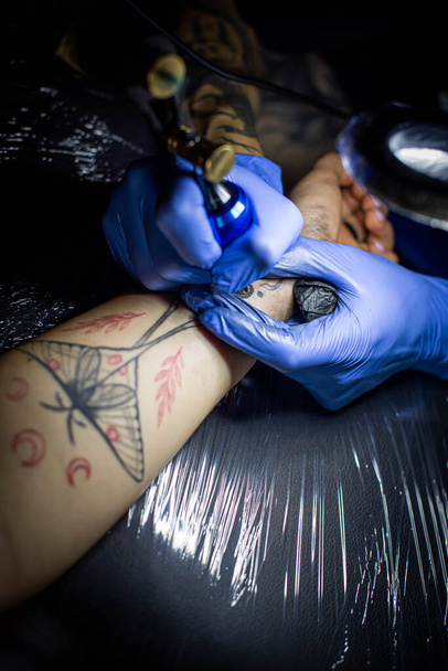tiro cortado de processo de tatuagem na mão no salão. Um tatuador profissional introduz tinta na pele usando uma agulha de uma máquina de tatuagem. Tatuagem profissional trabalhando em estúdio. - Foto, Imagem