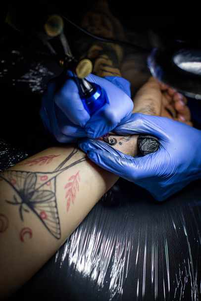 cropped shot of tattooing process on hand in salon. A professional tattoo artist introduces ink into the skin using a needle from a tattoo machine.Professional tattooist working in studio. - Valokuva, kuva
