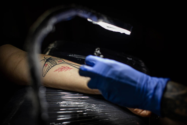 обрезанный снимок процесса татуировки под рукой в салоне. Профессиональный татуировщик вводит чернила в кожу с помощью иглы от татуировки.Профессиональный татуировщик работает в студии. - Фото, изображение